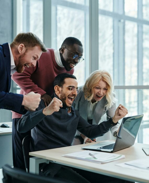 pexels-photo-7108959-7108959 A diverse team in an office celebrates a successful achievement while looking at a laptop.